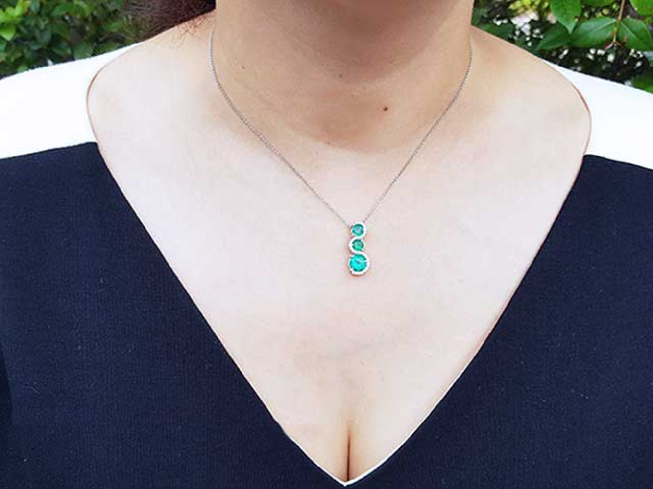 Necklace with a journey emerald pendant worn by a woman in a black top, against a blurred natural background.