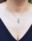 Necklace with a journey emerald pendant worn by a woman in a black top, against a blurred natural background.