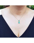 14K white gold emerald journey pendant necklace with three round deep green emeralds and diamonds.