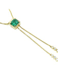 14K gold lariat necklace with a square emerald pendant and dangling diamond accents on a box chain.