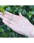 14K white gold "love" script pendant necklace with a round Colombian emerald, worn on a hand.