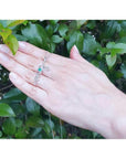 14K white gold "love" script pendant necklace with a round Colombian emerald, worn on a hand.