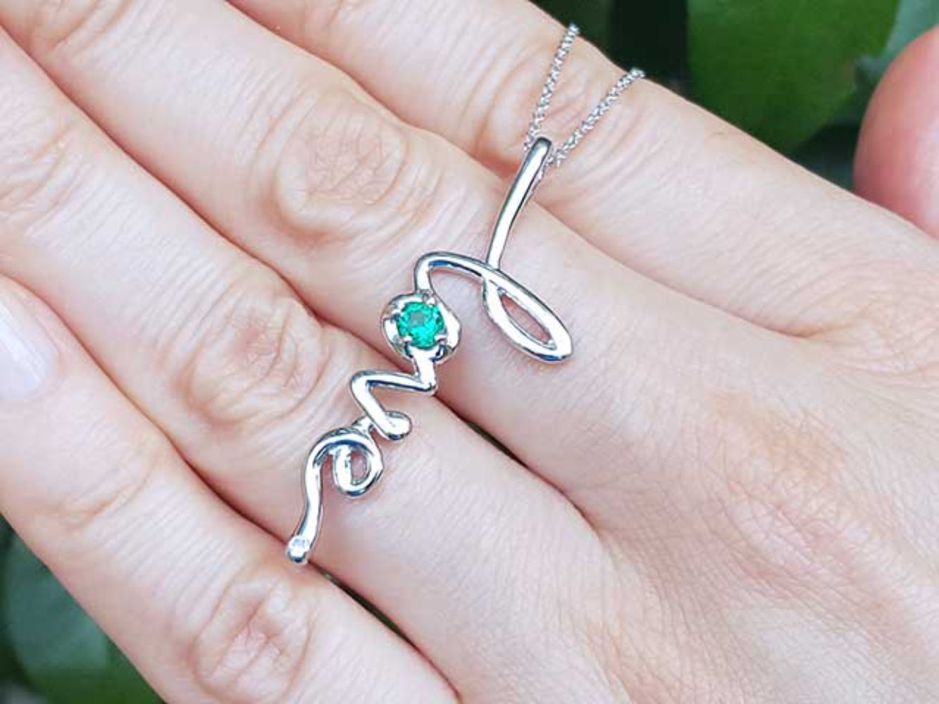 A 14K Solid gold emerald love pendant held between fingers.