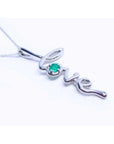 A 14k white gold necklace with a script love pendant featuring an emerald stone from Colombia.