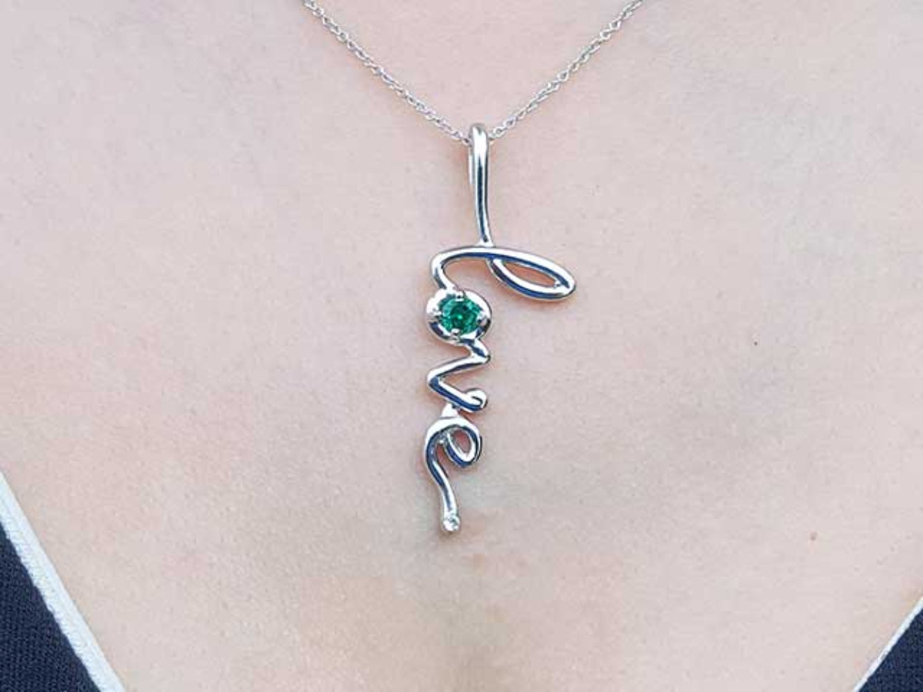 White gold necklace with 'love' pendant and natural emerald on a person's neck.