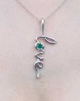 White gold necklace with 'love' pendant and natural emerald on a person's neck.