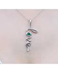 14K white gold "Love" script pendant necklace with a round cut Colombian emerald.