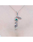 14K white gold "Love" script pendant necklace with a round cut Colombian emerald.
