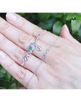 14K white gold "love" script pendant necklace with a round Colombian emerald, held on a hand.