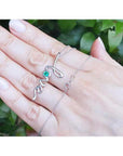 14K white gold "love" script pendant necklace with a round Colombian emerald, held on a hand.