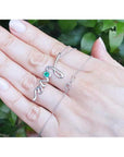 14K white gold "love" script pendant necklace with a round Colombian emerald, held on a hand.