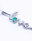 A white gold necklace with a script love pendant featuring an emerald stone on a white background.
