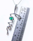 A white gold necklace with a round cut emerald love pendant next to a ruler for size reference.