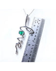 14K white gold "love" script pendant necklace with a round Colombian emerald, next to a ruler.