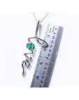14K white gold "love" script pendant necklace with a round Colombian emerald, next to a ruler.