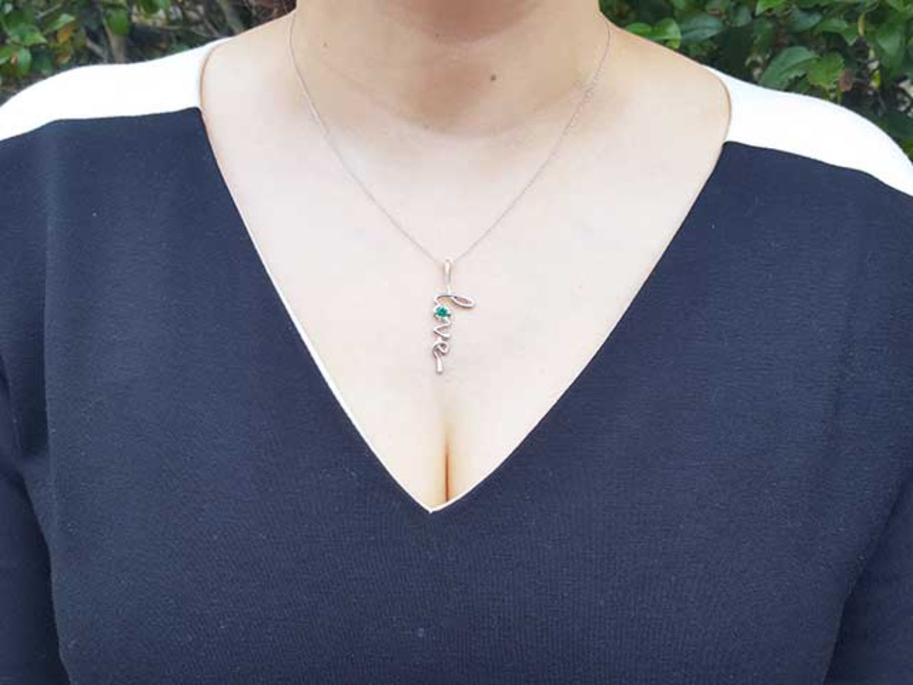 A woman wearing a dark blue top with a necklace featuring a love pendant.