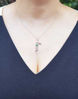 A woman wearing a dark blue top with a necklace featuring a love pendant.