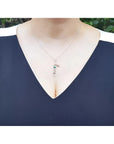 14K white gold "Love" script pendant with a round Colombian emerald, worn on a woman's neck.