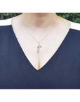14K white gold "Love" script pendant with a round Colombian emerald, worn on a woman's neck.