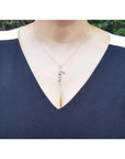 14K white gold "Love" script pendant with a round Colombian emerald, worn on a woman's neck.