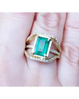 Emerald cut emerald engagement ring in 18K yellow gold with three rows of diamonds.