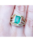 Emerald cut emerald engagement ring in 18K yellow gold with three rows of diamonds.