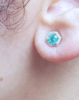 A close-up of a ear wearing a round cut emerald stud earring.