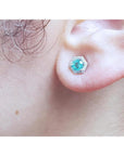 Emerald May birthstone stud earring in 14K white gold with a hexagonal halo on an earlobe.