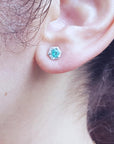 A woman's ear dressing a stud emerald earring with hexagonal halo diamond.