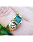 An 18k yellow gold men’s ring featuring a genuine Colombian emerald and side diamonds, elegantly worn on a finger.