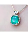 Cushion cut emerald necklace in 18K yellow gold with halo diamonds and a single diamond accent.