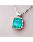 Cushion cut emerald necklace in 18K yellow gold with halo diamonds and a single diamond accent.