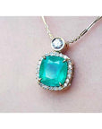 Cushion cut emerald necklace in 18K yellow gold with halo diamonds and a single diamond accent.