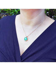 Cushion cut emerald necklace with halo diamonds in 18K yellow gold on a person.