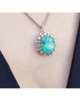 Oval cut medium light green emerald pendant with halo diamonds in 14K white gold on a necklace.