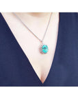 Oval cut emerald pendant with halo diamonds on a 14K white gold chain, worn on a woman's chest.