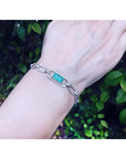 14K white gold paper clip bracelet with a rectangular emerald haloed by diamonds on a wrist.