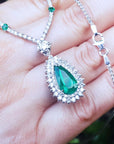 Closer view of a green teardrop emerald pendant with chain held in hand