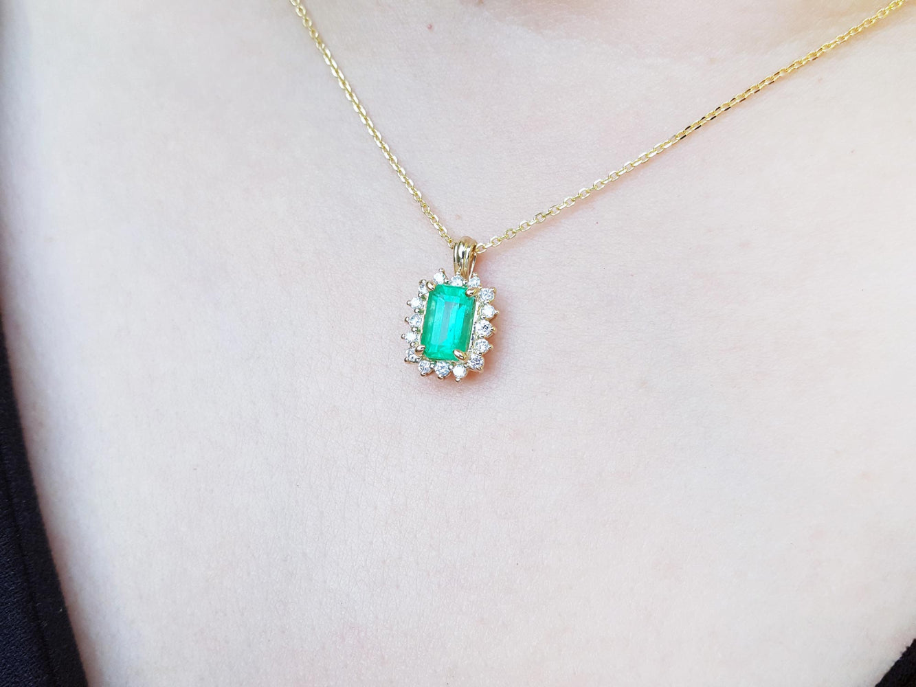 Gold necklace with a Muzo colombian emerald pendant on a person's neck.