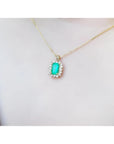 Emerald pendant with a halo of diamonds on a gold chain, worn on a person's chest.