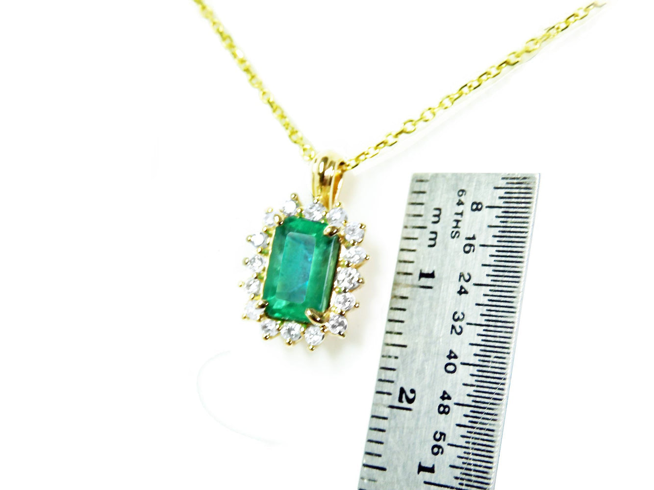 Gold necklace with an emerald pendant next to a ruler for scale on a white background.