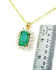 Gold necklace with an emerald pendant next to a ruler for scale on a white background.