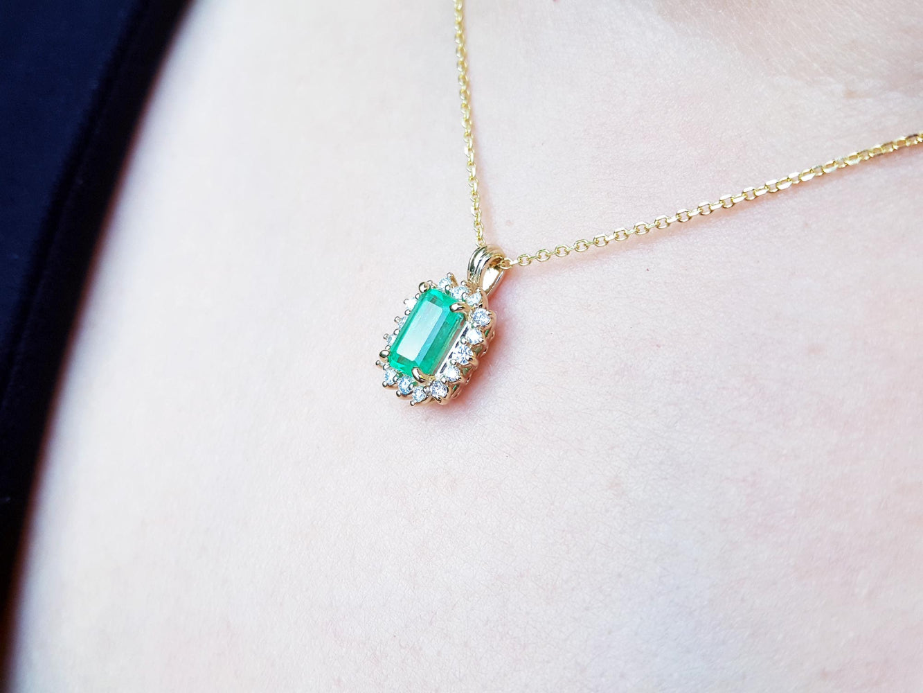 Gold necklace with a real colombian emerald pendant on a light pink skin background.