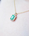 Gold necklace with a real colombian emerald pendant on a light pink skin background.