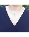 14K yellow gold pendant with a rectangular emerald surrounded by a diamond halo, worn on a woman's neck.