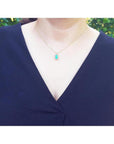 14K yellow gold pendant with a rectangular emerald surrounded by a diamond halo, worn on a woman's neck.