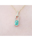 Gold necklace with a colombian emerald pendant on a light pink background.