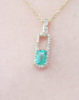 Gold necklace with a colombian emerald pendant on a light pink background.