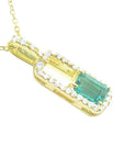 An emerald-cut Colombian emerald pendant with a halo of natural diamonds, handcrafted in 18K yellow gold.