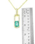 Gold necklace with a natural emerald pendant next to a ruler for size reference on a white background.